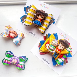 May include: Four hair bows featuring character-themed designs. Two large bows are mounted on Tini Bows cards, one with a cowgirl figure and one with space ranger and cowboy figures. Two smaller bows feature cartoon character prints and circular icons.