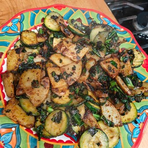 May include: A colorful plate of cooked vegetables, including sliced zucchini and potatoes, with dark green leafy greens. The food is arranged on a decorative plate with a red rim and a vibrant, multi-colored design.