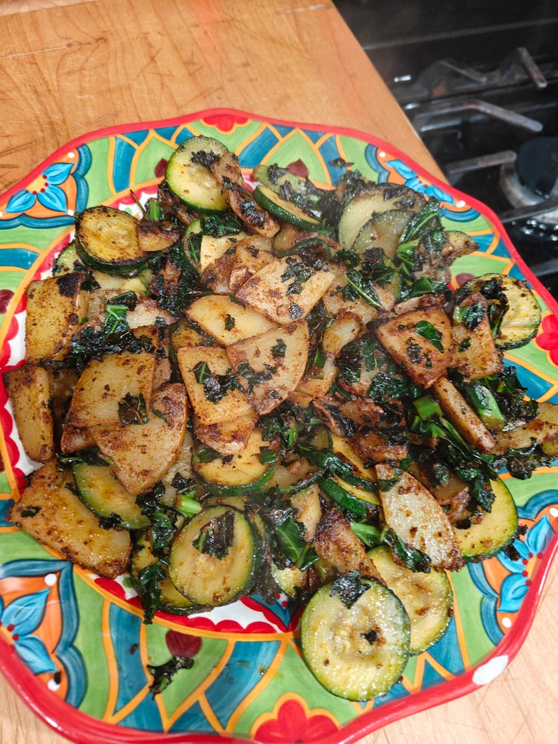 May include: A colorful plate of cooked vegetables, including sliced zucchini and potatoes, with dark green leafy greens. The food is arranged on a decorative plate with a red rim and a vibrant, multi-colored design.