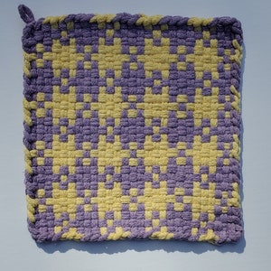 May include: A purple and yellow woven pot holder with a fringed edge.
