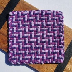 Peut inclure: Un dessous de plat tissé de couleur violet et lavande avec un motif géométrique.
