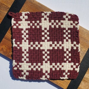 May include: A burgundy and white woven pot holder with a geometric pattern. The pot holder is made of a thick, durable material and is perfect for protecting your hands from hot surfaces.