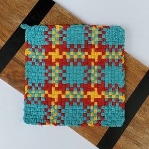 Puede incluir: Un posavasos tejido con un patrón geométrico en tonos de turquesa, rojo y amarillo.