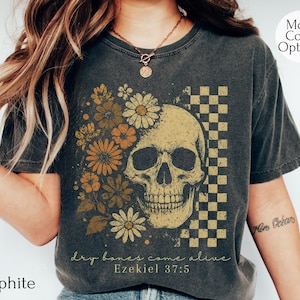 May include: Graphite-colored t-shirt featuring a skull design with floral accents and a checkered pattern. The design includes the text "dry bones come alive" and "Ezekiel 37:5". The shirt has a vintage, worn look.