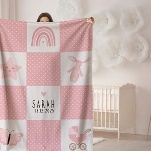 Puede incluir: Manta para bebé rosa y blanca con diseño de patchwork. La manta presenta un arcoíris, una estrella, un conejito, una mariposa y un cochecito. El nombre "Sarah" y la fecha "18.12.2025" están impresos.