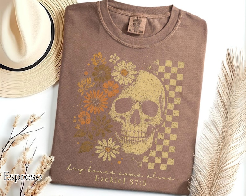 May include: Espresso-colored t-shirt featuring a skull design with floral accents and a checkered pattern. The graphic includes the text "dry bones come alive" and "Ezekiel 37:5". The shirt is a Comfort Colors XL-TG-BG.