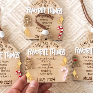 May include: Three wooden ornaments shaped like arched gingerbread houses with a candy cane and gingerbread man accents. Each ornament has a list of favorite things with a name and year. The ornaments read "These are a few of my favorite things" with the names Konrad 2024, Elora 2024, and Micah 2024.
