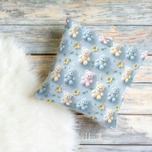 May include: A square pillow with a light blue background, covered in small teddy bear figures in pastel colors. The bears are beige, light blue, and pink, with small yellow flowers scattered around them. The pillow is on a wooden surface.