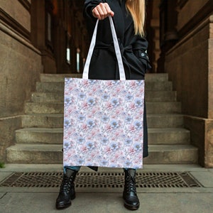 May include: A white tote bag with a floral pattern featuring pink and blue flowers. The bag has white straps.