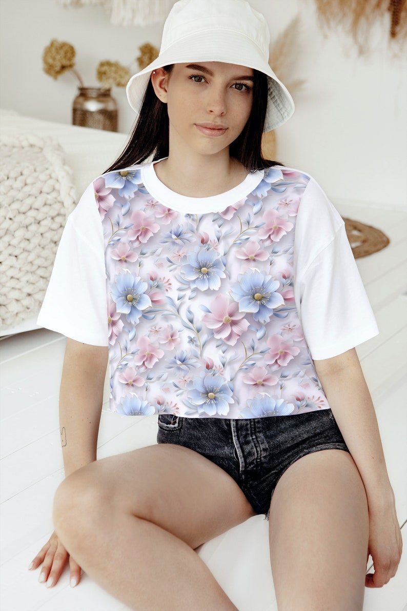 May include: A white cropped t-shirt with a floral print featuring pink and blue flowers. The shirt has short sleeves and a round neckline.