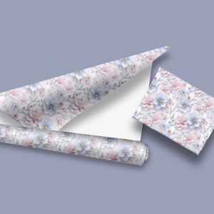 May include: A roll of floral patterned wrapping paper with pink and blue flowers. The paper is rolled up and partially unrolled, showing the pattern. There is also a small square of the same wrapping paper.