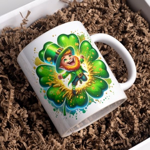 May include: White ceramic mug with a green four-leaf clover design. A cartoon leprechaun wearing a green hat and holding a pot of gold is jumping out of the clover.