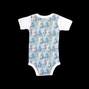 May include: Baby bodysuit with a pattern of small teddy bears in pastel colors on a light blue background. The bears are pink, blue, and cream-colored, with small yellow flower accents. The sleeves and neckline are white.