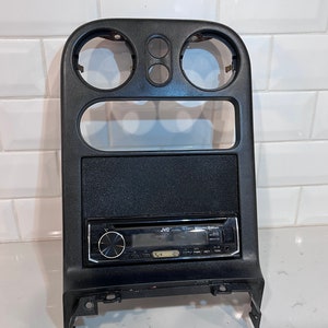May include: Black plastic car radio dash kit with three round openings and a rectangular opening for a radio. A black JVC radio is installed in the kit.