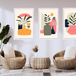 Peut inclure: Trois impressions d'art abstraites encadrées avec des motifs colorés de vases et de plantes. Les impressions présentent des formes orange, rose, bleu et vert. Deux chaises en osier et une table ronde sont devant les impressions.