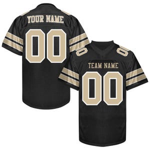 Puede incluir: Camiseta de f&uacute;tbol negra con detalles dorados y blancos. La camiseta muestra el n&uacute;mero "00" en dorado con un contorno blanco en la parte delantera y trasera. La parte trasera de la camiseta tiene el texto "YOUR NAME" encima del n&uacute;mero.
