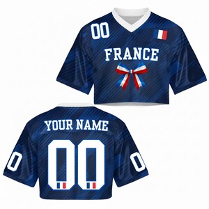 May include: A blue crop top jersey with the word "FRANCE" in white block letters, a bow in the colors of the French flag, and the number "00" in white. The back of the jersey has the text "YOUR NAME" and the number "00".