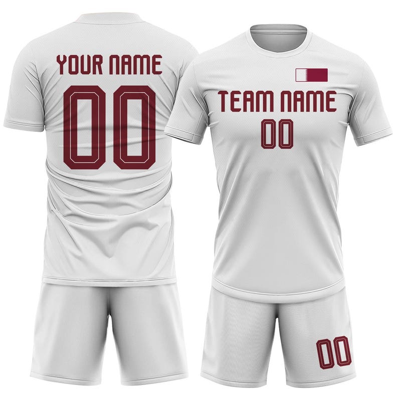 Op de afbeelding: Witte voetbaltenue met bordeauxrode accenten. Het shirt heeft "YOUR NAME" en het nummer "00" op de rug, en "TEAM NAME" en het nummer "00" op de voorkant. Inclusief bijpassende shorts.