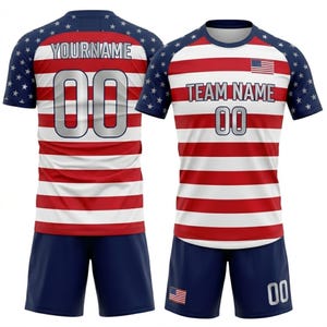 May include: A red and white striped soccer uniform with blue shorts. The jersey has blue sleeves with white stars and the text "YOURNAME" and "TEAM NAME" above the number "00". An American flag is on the jersey.