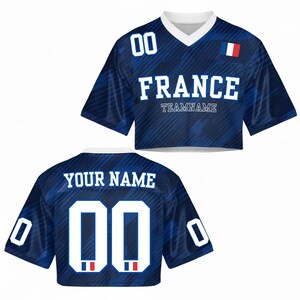 May include: A blue crop top jersey with the word "FRANCE" in white block letters and the number "00". The jersey has a V-neck collar and a small French flag patch. The back of the jersey says "YOUR NAME" and has the number "00".