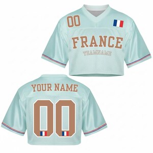 May include: A light blue cropped jersey with the word "FRANCE" in brown block letters. The jersey has the number "00" on the front and back, with the French flag and the text "YOUR NAME" on the back. The sleeves have red and blue stripes.