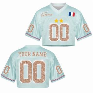 May include: Light blue crop top jersey with the word "France" in cursive and the number "00" in glitter. Features a French flag and two gold stars. The back of the jersey says "YOUR NAME" and has the number "00".