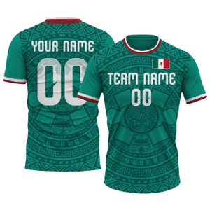 Op de afbeelding: Twee groene voetbalshirts met witte letters en het nummer 00. E&eacute;n shirt heeft "YOUR NAME" op de rug, de andere heeft "TEAM NAME". Beide hebben een Mexicaanse vlag en door Azteken ge&iuml;nspireerde patronen. De shirts hebben rode en witte afwerking.