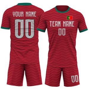 Op de afbeelding: Een rood voetbaltenue met een golvend patroon, met de tekst "YOUR NAME" en "TEAM NAME" in het wit. Het nummer "00" staat op de voor- en achterkant van het shirt. Het tenue bevat een Portugese vlag.
