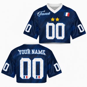 May include: A cropped blue jersey with the word "France" in script and the number "00" in white. The jersey has a white V-neck collar, two gold stars, and a French flag emblem. The back of the jersey says "YOUR NAME" and has the number "00".