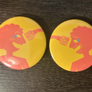 May include: Two yellow round badges with a red illustration of a person. One badge says "BEST WISH MASTER" and the other says "BEST WORLD BUILDER". The badges have a retro design.