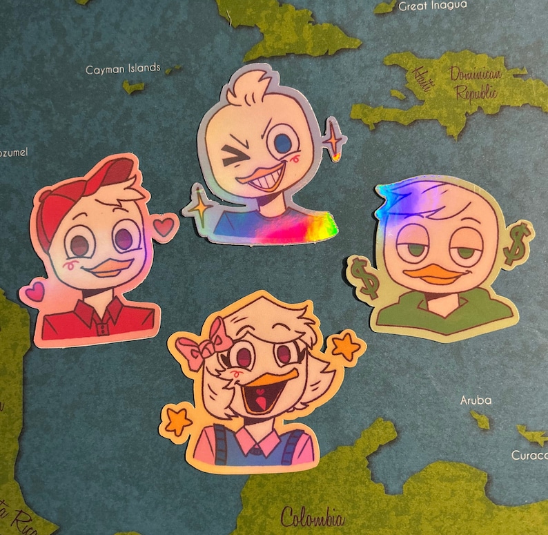 May include: Four holographic stickers featuring cartoon ducks with different expressions. The ducks are wearing different outfits, including a red shirt, a blue shirt, a green shirt, and a pink shirt. The stickers are on a map background.
