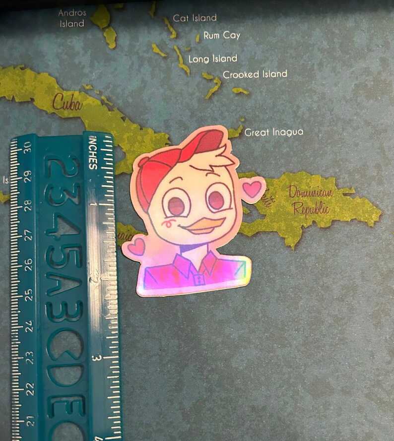 May include: A holographic sticker of a cartoon duck wearing a red baseball cap and a red and blue plaid shirt. The duck has a pink blush on its cheeks and is holding a pink heart in its hand. The sticker is on a map of the Caribbean.