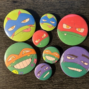 May include: Set of nine Teenage Mutant Ninja Turtles themed buttons. The buttons feature different characters from the show, including Leonardo, Donatello, Raphael, and Michelangelo. The buttons are all round and have a green, red, blue, purple, or orange background.