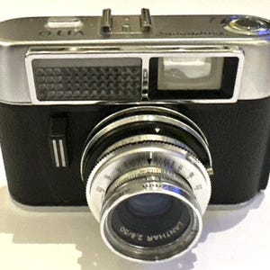May include: A vintage black and silver camera with a prominent lens. The lens is labeled 'Lanthar 2.8/50'. The camera has a silver top and a black body. The word 'Vito' is visible on the top of the camera.