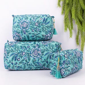 May include: Three quilted cosmetic bags in varying sizes. The bags feature a teal floral pattern with blue and white accents. Each bag has a teal tassel and gold-colored zipper pull. The bags are arranged on a white surface.
