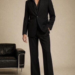 May include: A black suit consisting of a single-breasted blazer with a notched lapel and matching wide-leg trousers. The blazer features a single button closure and patch pockets. The text Falcon's Era is visible in the upper right corner.
