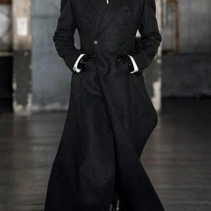 Pu&ograve; includere: Un lungo cappotto nero doppiopetto con una vestibilit&agrave; su misura. Il cappotto presenta un colletto alto, una camicia bianca e una cravatta nera. Il modello indossa guanti neri e scarpe nere. Il cappotto &egrave; lungo fino al pavimento.