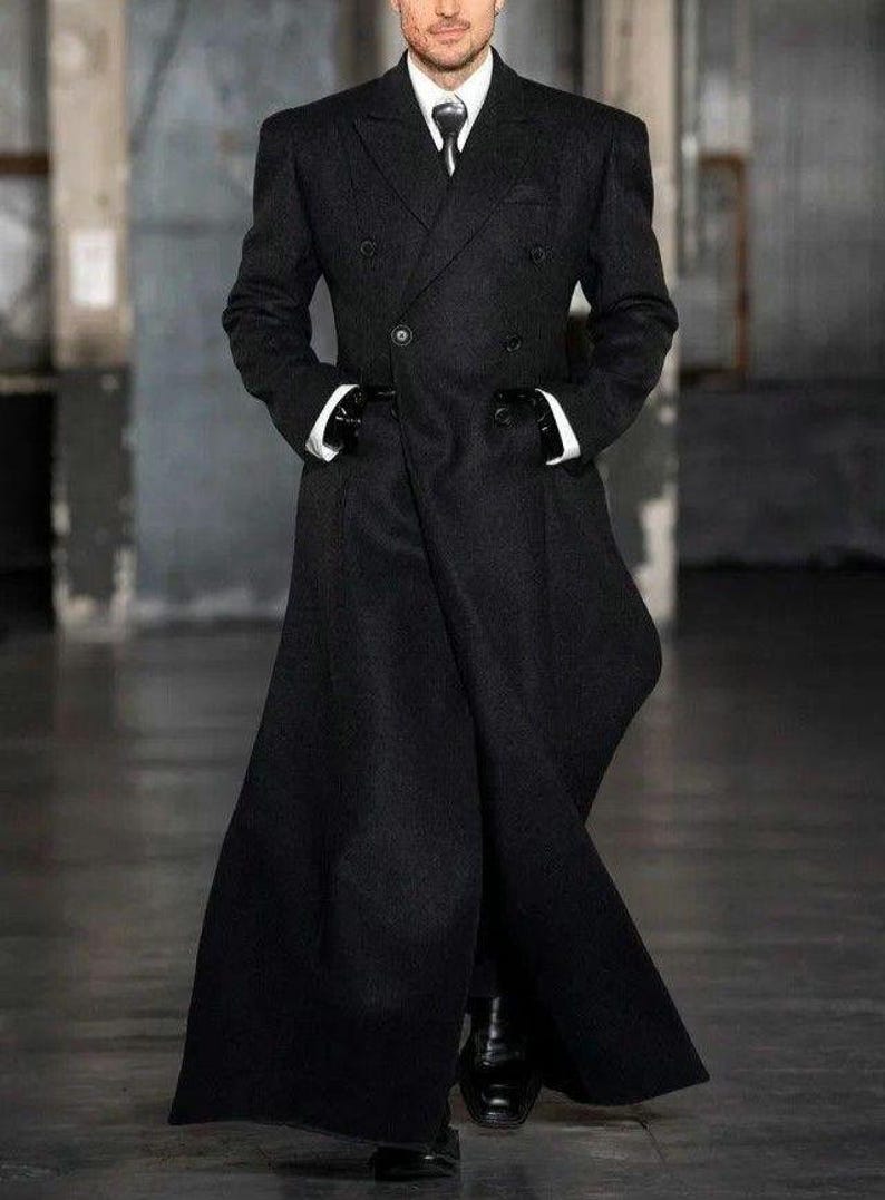 Pu&ograve; includere: Un lungo cappotto nero doppiopetto con una vestibilit&agrave; su misura. Il cappotto presenta un colletto alto, una camicia bianca e una cravatta nera. Il modello indossa guanti neri e scarpe nere. Il cappotto &egrave; lungo fino al pavimento.