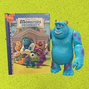 May include: A Disney Pixar Monsters University hardcover book featuring a group of animated characters on the cover, positioned next to a blue, furry-textured plastic action figure of the character James P. Sullivan with purple spots.