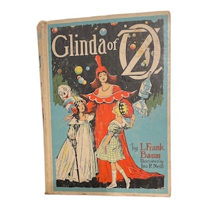 May include: A hardcover book titled Glinda of Oz by L. Frank Baum, illustrated by Jno R. Neill. The cover features a colorful illustration of Glinda in a red gown, a girl in a white dress, a girl in a green checkered dress, a robot, and a clown.