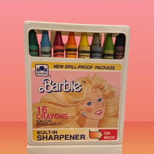 May include: A white crayon box featuring the Barbie logo and a portrait of Barbie. The box contains 16 crayons in various colors. The text "Built-in Sharpener" is visible on the box. The package is labeled "New Spill-Proof Package."