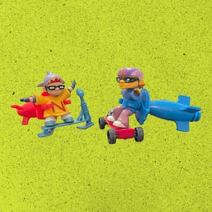 May include: Two toy figures on a bright yellow-green background. One figure is on a blue scooter, wearing a yellow jacket with a red rocket. The other figure is on a red skateboard with a blue jetpack. Both figures have goggles and helmets.