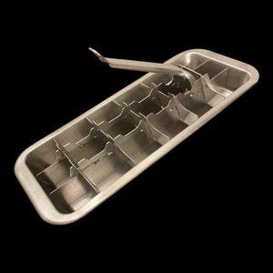 May include: A rectangular silver-colored metal ice cube tray featuring a built-in lever mechanism. The tray is constructed with a series of internal dividers to create individual compartments for freezing water into ice cubes, with a handle attached.