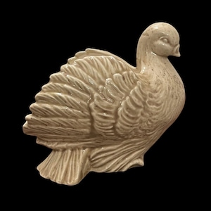May include: A cream-coloured ceramic bird figurine, possibly a dove or pigeon, with speckled detailing. The bird is shown in profile, with textured feathers and a slightly open beak. The figurine has a rounded body and a small tail, and is likely a decorative item.