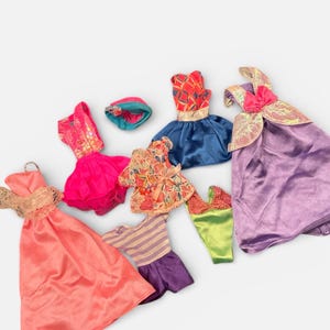 May include: A collection of doll clothes in various styles and colors. The garments include dresses, tops, and skirts in shades of pink, purple, blue, and green. Some pieces have decorative details like lace and bows.