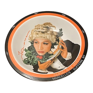 Puede incluir: Bandeja redonda con diseño retro. La bandeja presenta a una mujer con cabello rubio sosteniendo un plato de verduras. La bandeja tiene un borde naranja y negro con el texto "CIUFOLI ALLE VERDURE MARCELLO'S - SUFFERN, NY."