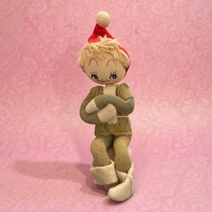 May include: A vintage doll with a red Santa hat and blonde yarn hair. The doll wears a green jacket, pants, and white boots. Its arms are crossed, and it has a sweet, painted face. The doll is a charming holiday decoration.
