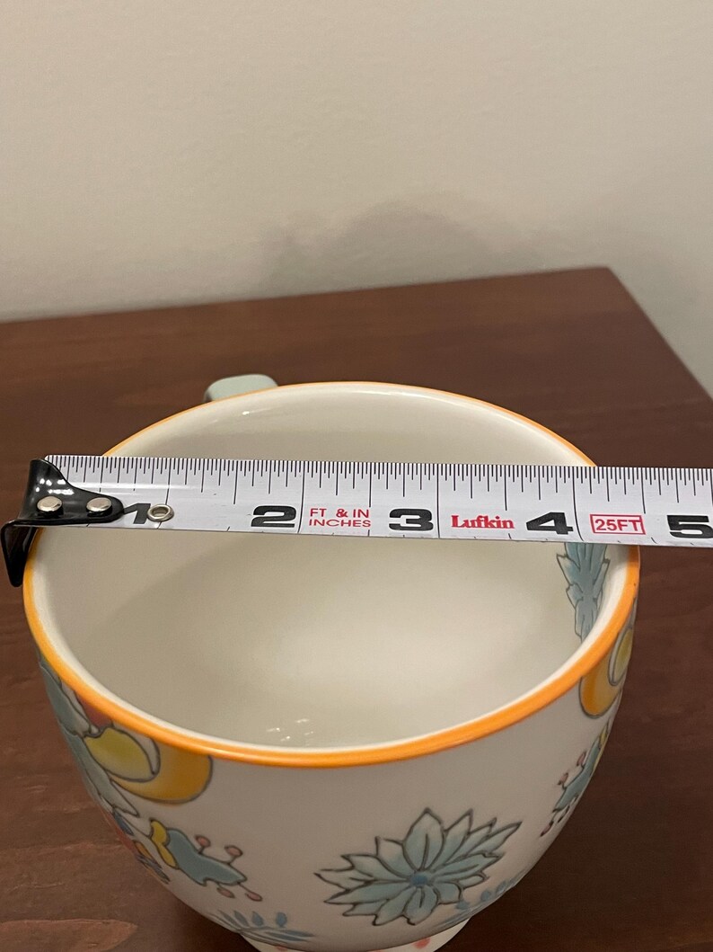 May include: White ceramic bowl with floral patterns in blue, yellow, and green, and an orange rim. The bowl's diameter is approximately 4 inches. A measuring tape is placed across the bowl.