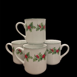May include: Set of four white ceramic mugs with a green holly and red berry design. The mugs have a green rim.