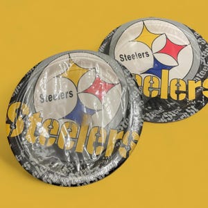 May include: Two paper plates featuring the Pittsburgh Steelers logo, with a white background and a black and gray border. The logo includes a yellow star, a red star, and a blue star. The word "Steelers" is printed on the plates.